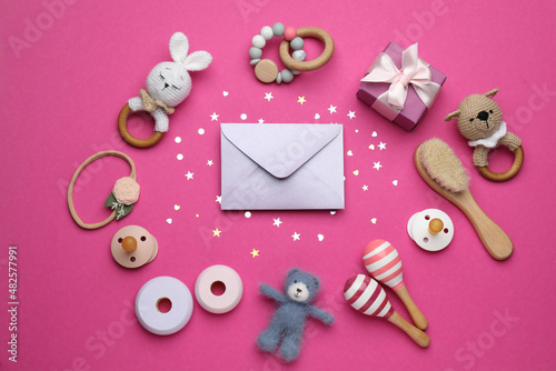 Baby shower party. Envelope surrounded by gift box, toys and accessories for child on bright pink background, flat lay