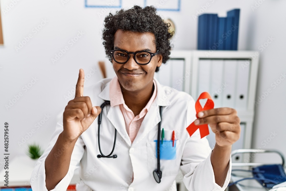 African doctor man holding support red ribbon surprised with an idea or question pointing finger with happy face, number one African doctor man holding support red ribbon surprised with an idea or question pointing finger with happy face, number one