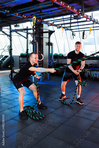 Athletic man doing exercises with the help of his personal trainer in a public gym.