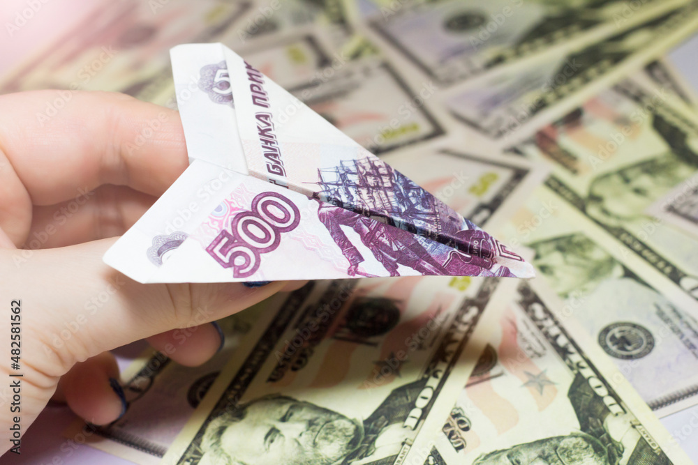 A plane made of a 500-ruble bill in a woman's hand. Dollar background.