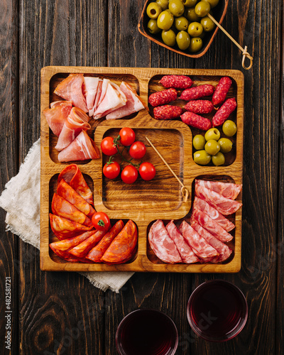 Snacks for wine on a wooden board. Menazhnitsa with sausage, olives and cherry tomatoes.