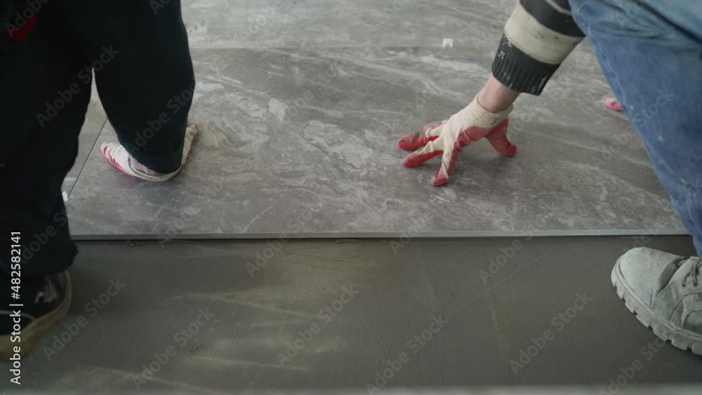 Workers are laying the floor with large tiles. A worker puts a large tile on the floor. Workers are installing a large ceramic tile on the floor.
