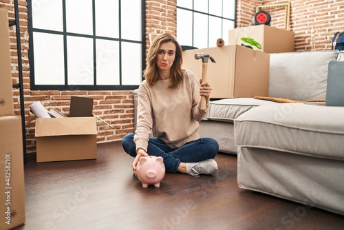 Young woman holding piggy bank and hammer moving to a new home depressed and worry for distress, crying angry and afraid. sad expression.