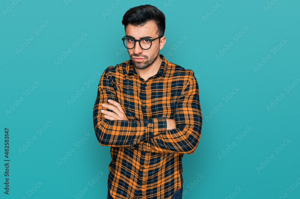 Hispanic man with beard wearing casual clothes and glasses skeptic and nervous, disapproving expression on face with crossed arms. negative person. Hispanic man with beard wearing casual clothes and glasses skeptic and nervous, disapproving expression on face with crossed arms. negative person.