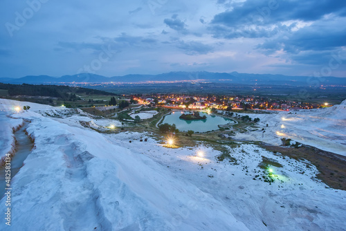 Pamukkale travertines in foreground. Sunset sky and illuminated houses