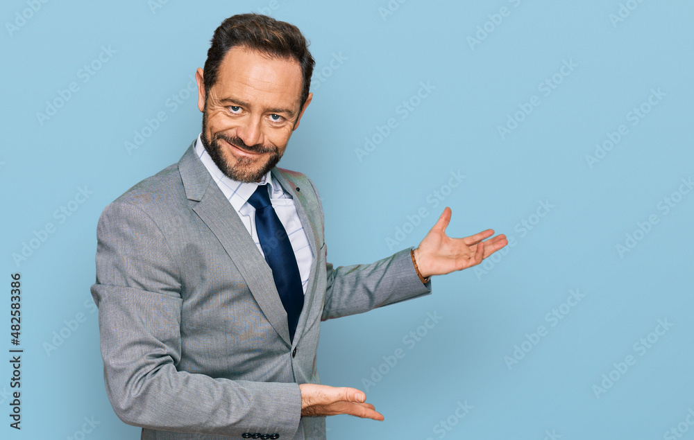 Middle age man wearing business clothes inviting to enter smiling natural with open hand Middle age man wearing business clothes inviting to enter smiling natural with open hand