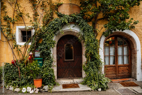 Hallstatt, Austria, 27 August 2021: Colorful scenic picturesque town street at summer day, oval wooden door, braided window, green ivy at yellow wall, traditional historical house, village near lake