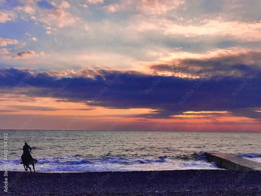 Stunning seascape. The rider on a horse at sunset on the beach. The person horse riding.