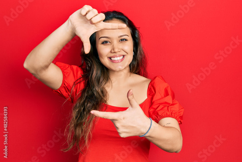 Obraz na plátně Young hispanic girl wearing casual clothes smiling making frame with hands and fingers with happy face