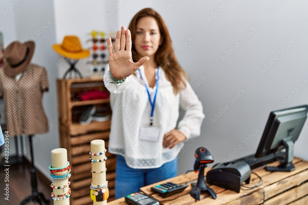 Middle age hispanic woman working as manager at retail boutique doing stop sing with palm of the hand. warning expression with negative and serious gesture on the face. Middle age hispanic woman working as manager at retail boutique doing stop sing with palm of the hand. warning expression with negative and serious gesture on the face.