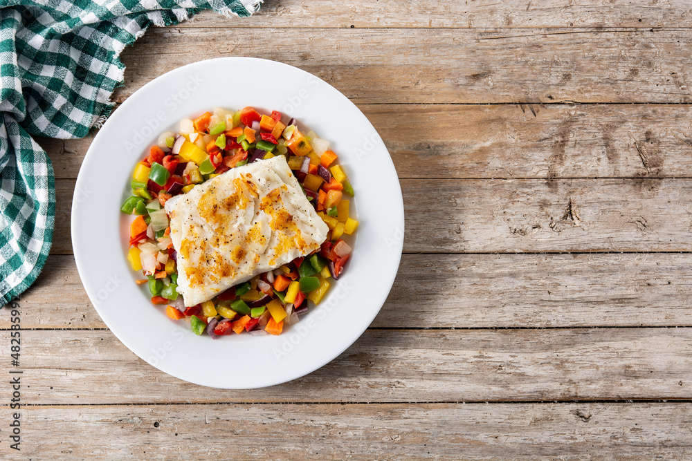 Grilled cod with vegetables in plate on wooden table. Top view. Copy space Grilled cod with vegetables in plate on wooden table. Top view. Copy space