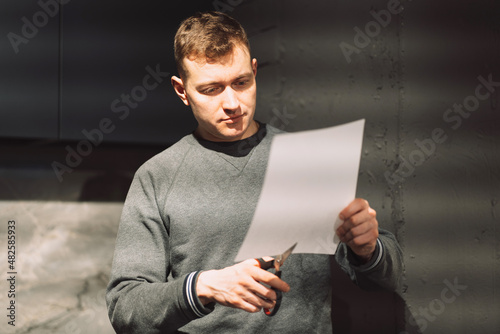 a man cuts a white sheet of paper with scissors from the bottom up