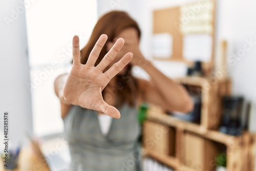 Middle age hispanic woman at the office covering eyes with hands and doing stop gesture with sad and fear expression. embarrassed and negative concept.