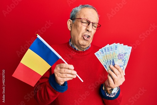 Handsome senior man with grey hair holding romania flag and leu banknotes depressed and worry for distress, crying angry and afraid. sad expression.