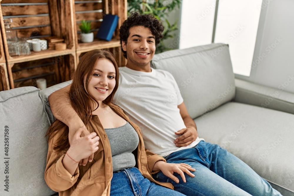 Obraz premium Young couple smiling happy and hugging sitting on the sofa at home.