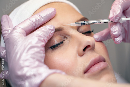 Close up careful master beautician who injects Botox in the brow area of ​​a young beautiful patient. Beauty treatment concept