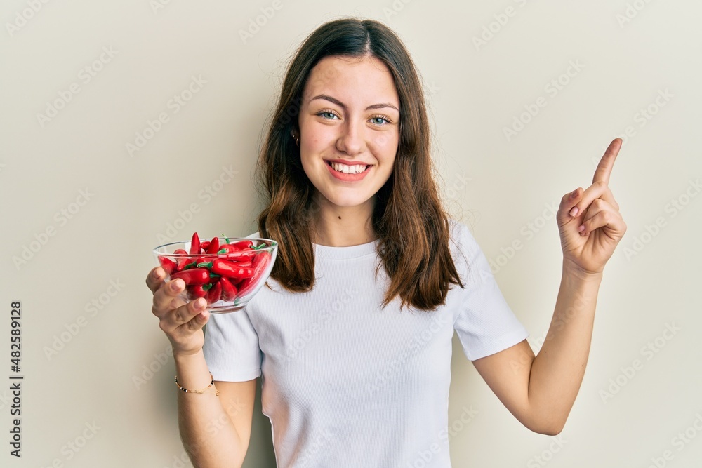 Young brunette woman holding red peppers smiling happy pointing with hand and finger to the side Young brunette woman holding red peppers smiling happy pointing with hand and finger to the side