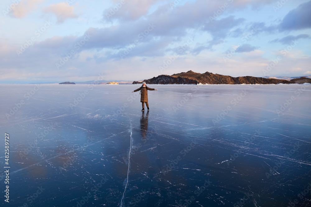 A happy young woman walks on the transparent ice of Lake Baikal. Beautiful landscape of frozen Lake Baikal at sunset. Travel in winter , active recreation. 