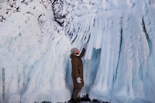 A woman looks at the huge icicles on the rocks of the island of Oltrek. Winter trip on Lake Baikal.  photo