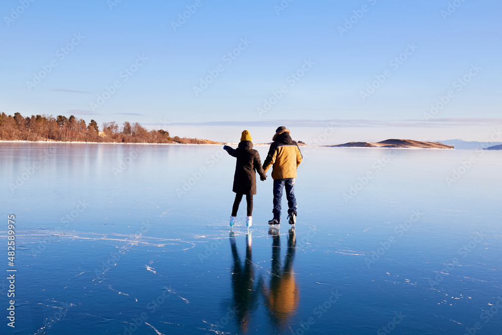 A young couple is skating on the frozen Lake Baikal. Transparent ice. Travel in winter, active recreation, sports. 