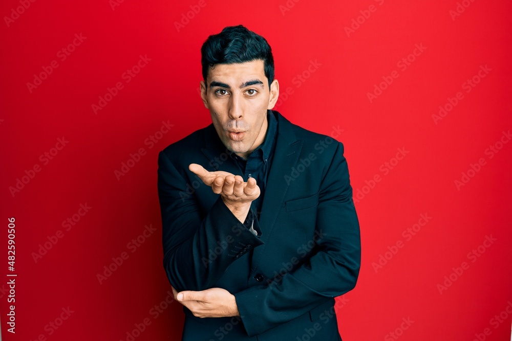 Handsome hispanic man wearing business clothes looking at the camera blowing a kiss with hand on air being lovely and sexy. love expression. Handsome hispanic man wearing business clothes looking at the camera blowing a kiss with hand on air being lovely and sexy. love expression.