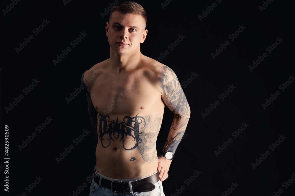 Shirtless young man with tattoos on black background Shirtless young man with tattoos on black background
