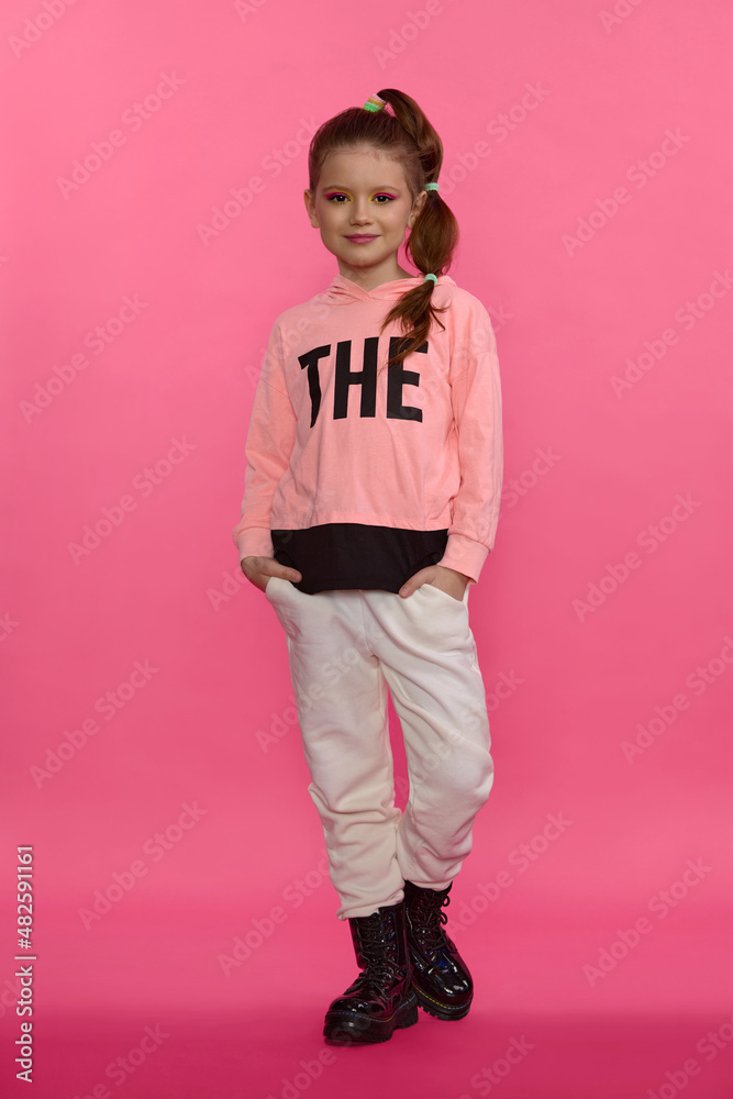 girl in a pink sweater and black shoes posing in the studio on a pink background 