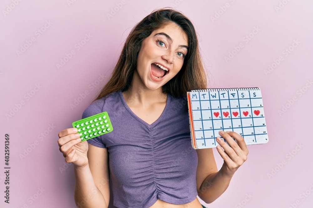 Young caucasian woman holding birth control pills and menstrual calendar celebrating crazy and amazed for success with open eyes screaming excited. Young caucasian woman holding birth control pills and menstrual calendar celebrating crazy and amazed for success with open eyes screaming excited.