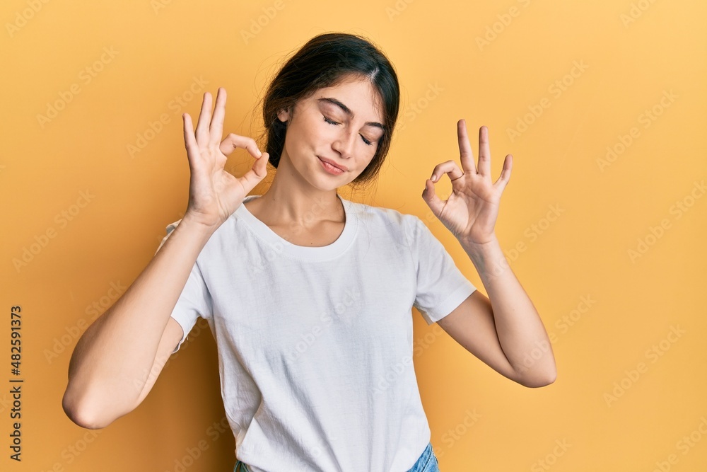 Young caucasian woman wearing casual white t shirt relax and smiling with eyes closed doing meditation gesture with fingers. yoga concept. Young caucasian woman wearing casual white t shirt relax and smiling with eyes closed doing meditation gesture with fingers. yoga concept.