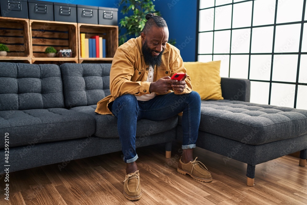 Young african american man using smartphone sitting on sofa at home