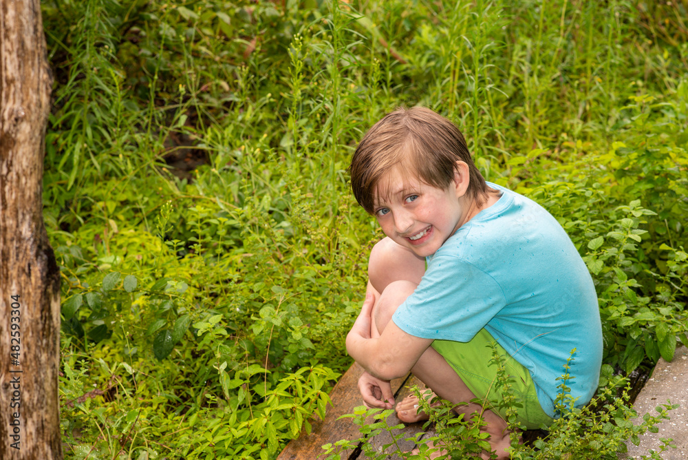 a little boy sits on a plank in the garden among green plants in summer
a little boy sits on a plank in the garden among green plants in summer