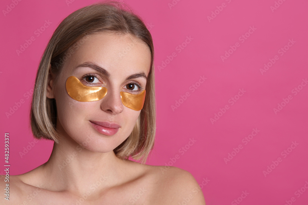 Beautiful young woman with under eye patches on pink background, space for text