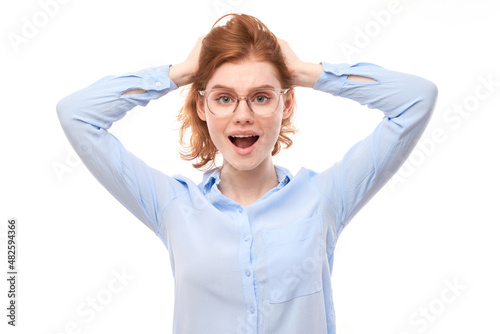 Shocked face ginger girl in business shirt looks surprised with open mouth holding head with hands on white studio background