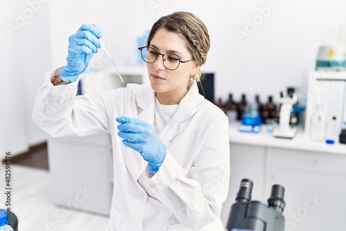 Young hispanic woman wearing scientist uniform using pipette at laboratory
