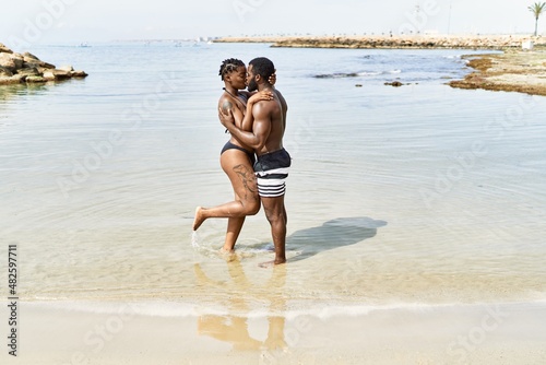 Young african american tourist couple wearing swimwear kissing and hugging at the beach.