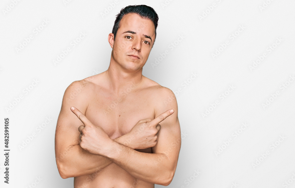 Handsome young man wearing swimwear shirtless pointing to both sides with fingers, different direction disagree Handsome young man wearing swimwear shirtless pointing to both sides with fingers, different direction disagree