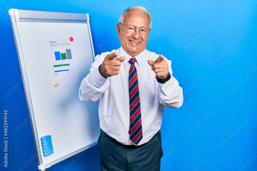 Senior man with grey hair standing by business blackboard pointing fingers to camera with happy and funny face. good energy and vibes. Senior man with grey hair standing by business blackboard pointing fingers to camera with happy and funny face. good energy and vibes.