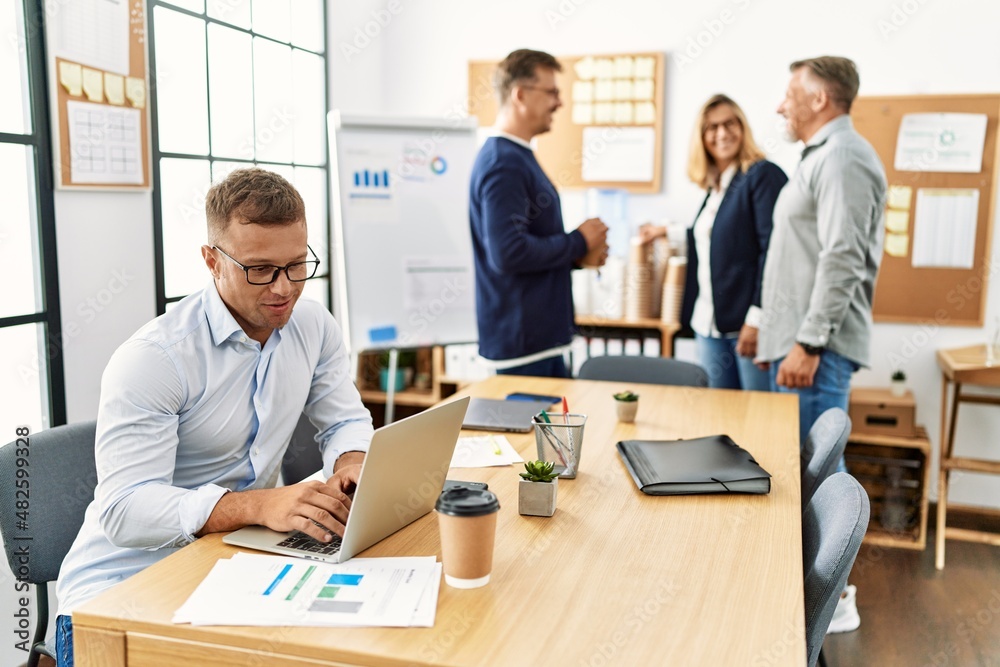 Middle age business worker smiling happy working while partners have break time at the office. Middle age business worker smiling happy working while partners have break time at the office.