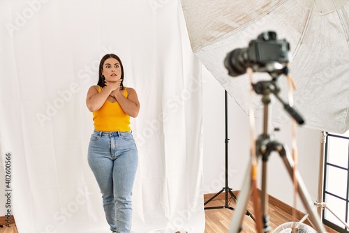 Young beautiful hispanic woman posing as model at photography studio shouting and suffocate because painful strangle. health problem. asphyxiate and suicide concept.