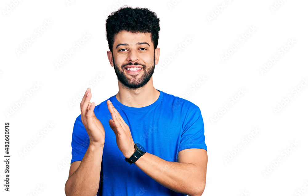 Young arab man with beard wearing casual blue t shirt clapping and applauding happy and joyful, smiling proud hands together Young arab man with beard wearing casual blue t shirt clapping and applauding happy and joyful, smiling proud hands together