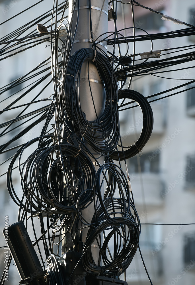 A lot of internet, communication and electricity cable hanged on a concrete pillar. Messy cables in the city.