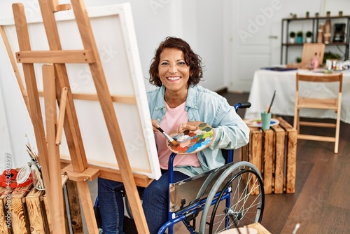 Billede på lærred Middle age hispanic disabled artist woman drawing sitting on wheelchair at art studio