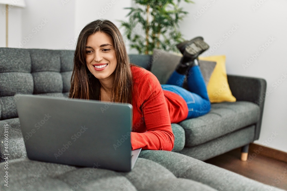 Young woman using laptop lying on sofa at home Young woman using laptop lying on sofa at home