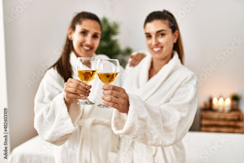 Two women wearing bathrobe toasting with champagne standing at beauty center