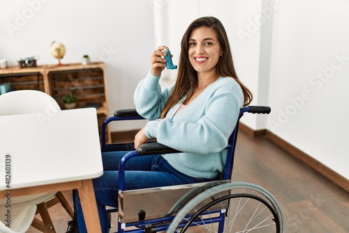Young woman using inhaler sitting on wheelchair at home