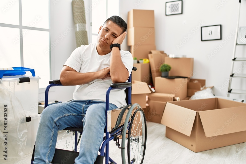 Young hispanic man sitting on wheelchair at new house thinking looking tired and bored with depression problems with crossed arms.