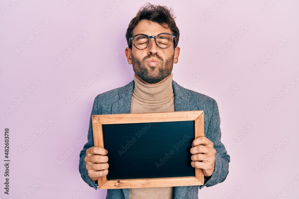 Handsome man with beard holding blackboard looking at the camera blowing a kiss being lovely and sexy. love expression. Handsome man with beard holding blackboard looking at the camera blowing a kiss being lovely and sexy. love expression.