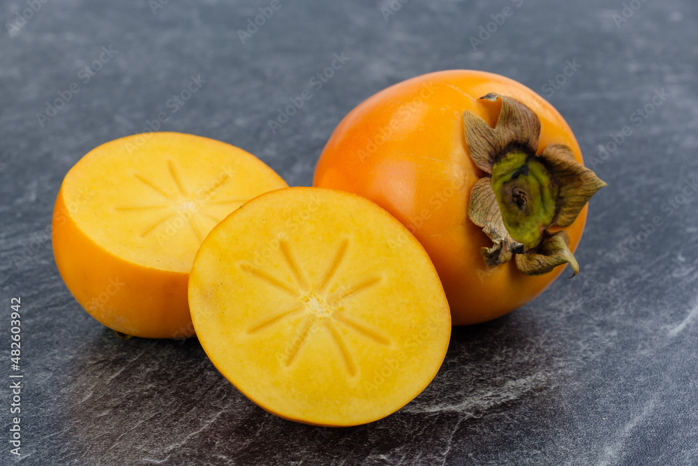 Orange, saftige tropische Kaki Früchte (lat.: Diospyros kaki) - eine davon ist aufgeschnitten
