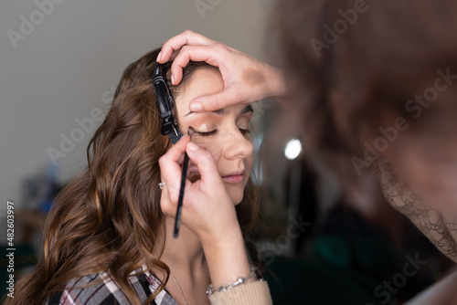 The makeup artist applies eyeliner to the girl with a brush on the upper eyelid and draws an arrow