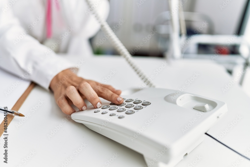 Fototapeta premium Young hispanic woman wearing doctor uniform talking on the telephone at clinic